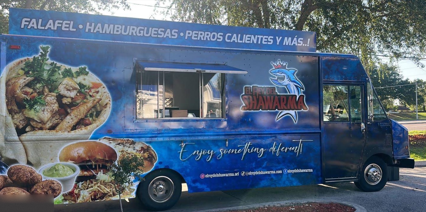 El Rey Del Shawarma brightly illuminated food truck at night in Orlando with smiling customers dining at outdoor picnic tables under string lights